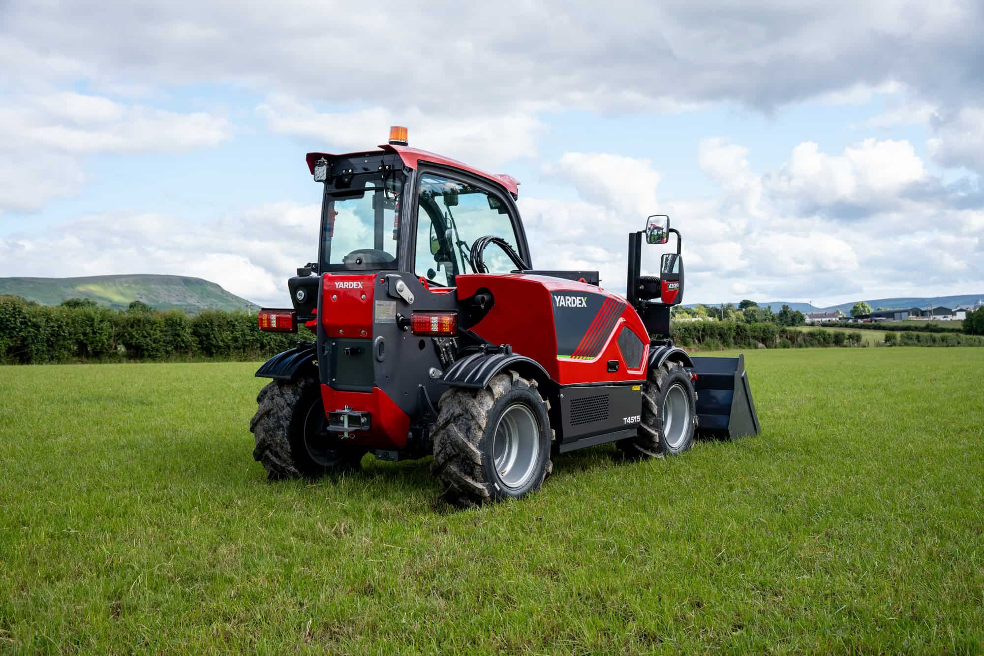 Red and black Yardex Group compact utility loader on green field.