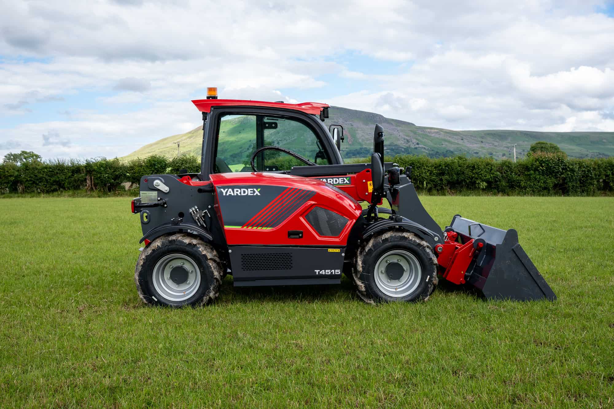 Yardex Group compact loader working on a grassy field with hills in the background.