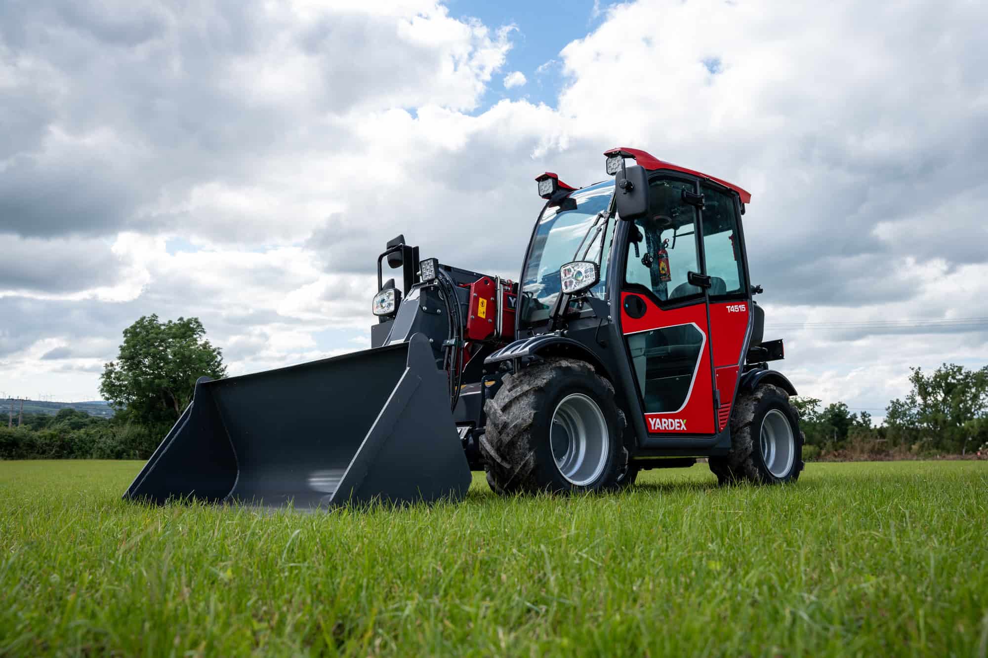 Yardex Group compact loader working on green field under cloudy sky.