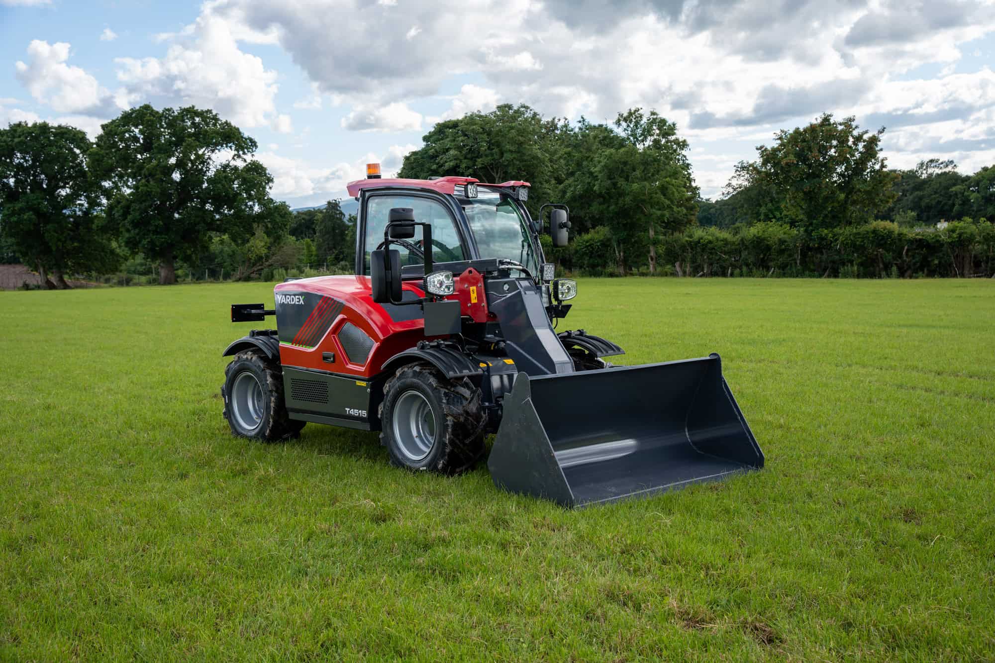 Yardex Group compact loader on green grass with trees and blue sky.