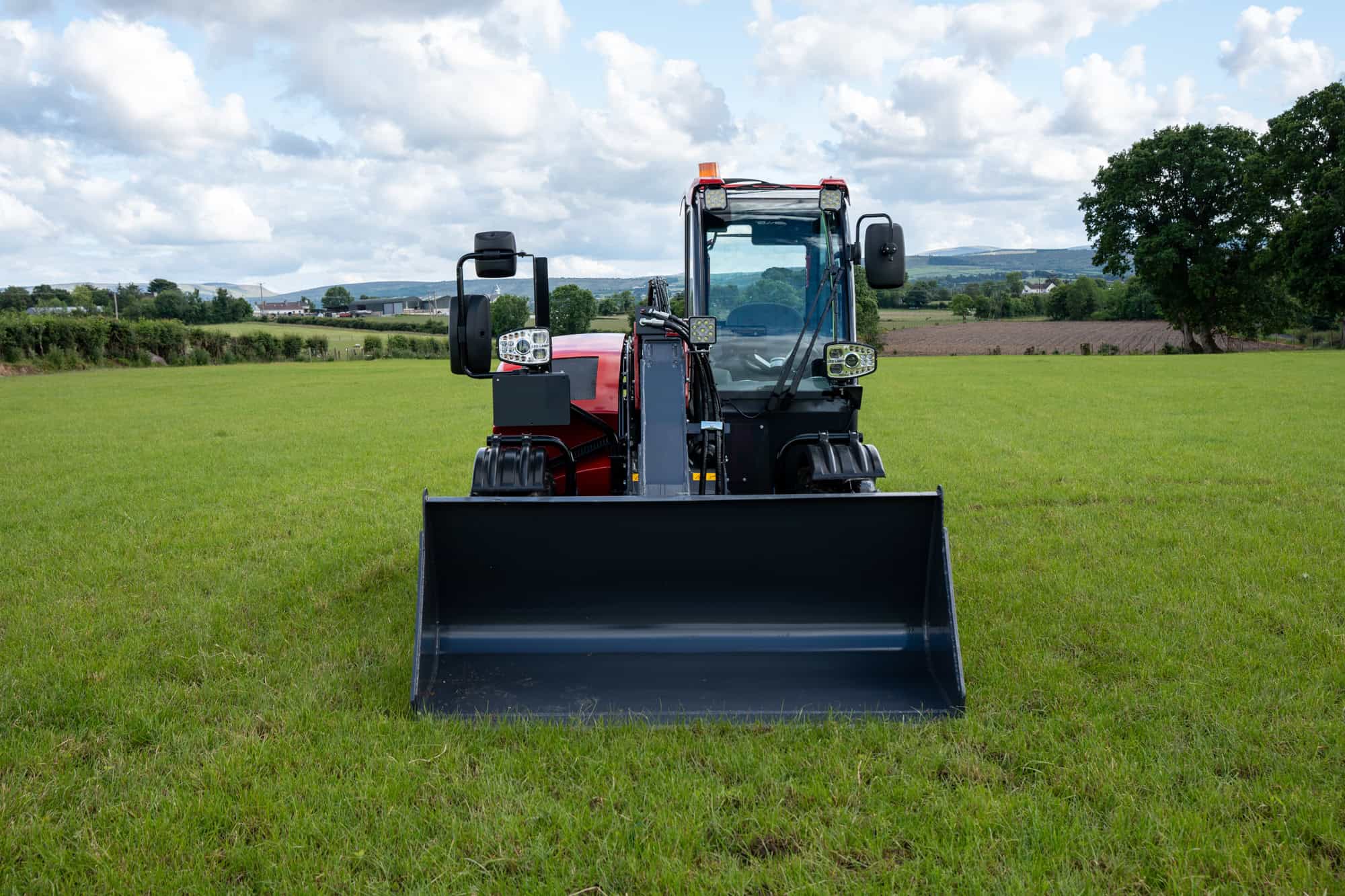Compact tractor with front loader on green field for landscaping.