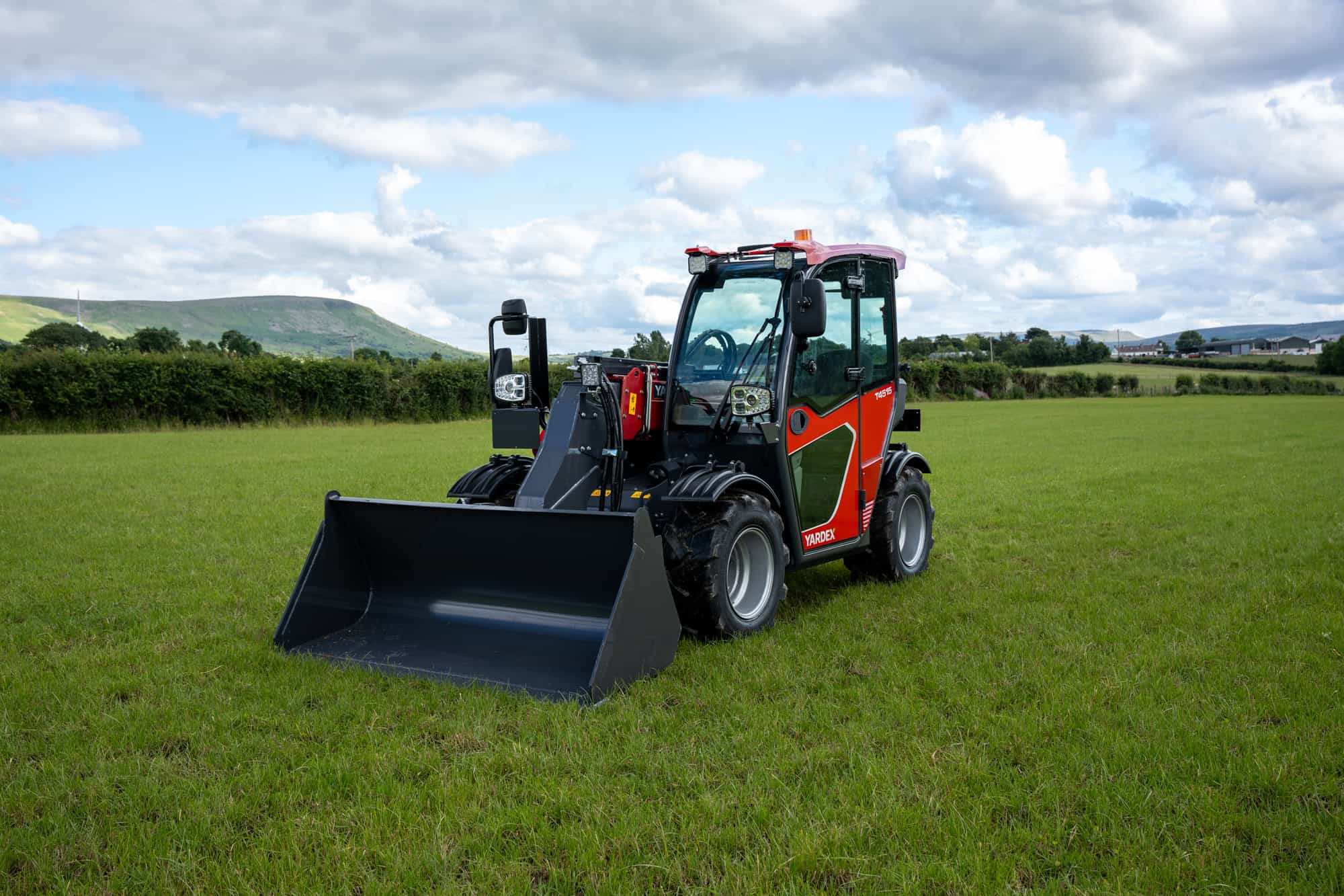 Yardex Group compact loader with bucket on green field under blue sky.