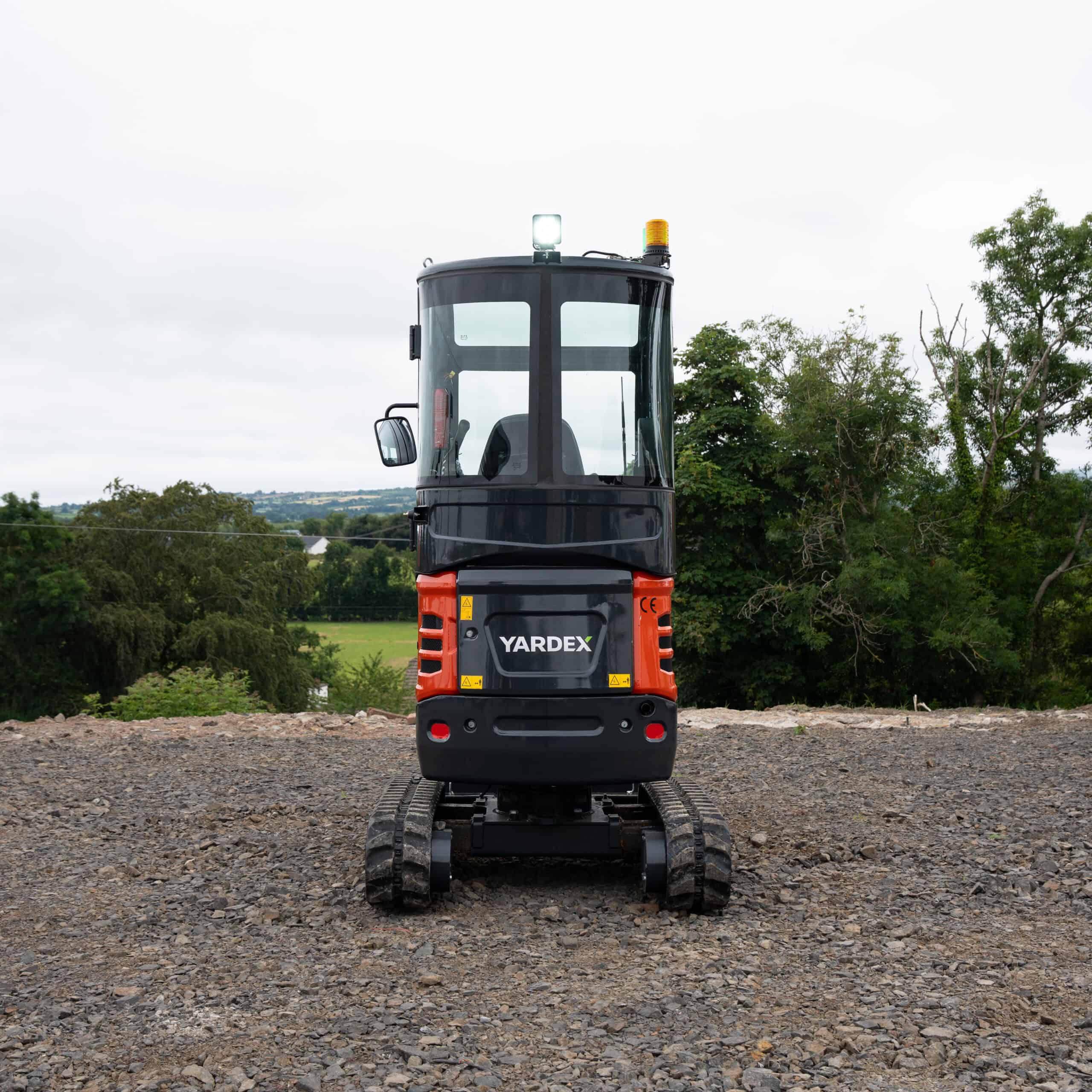Yardex Group compact excavator on construction site with green landscape background.