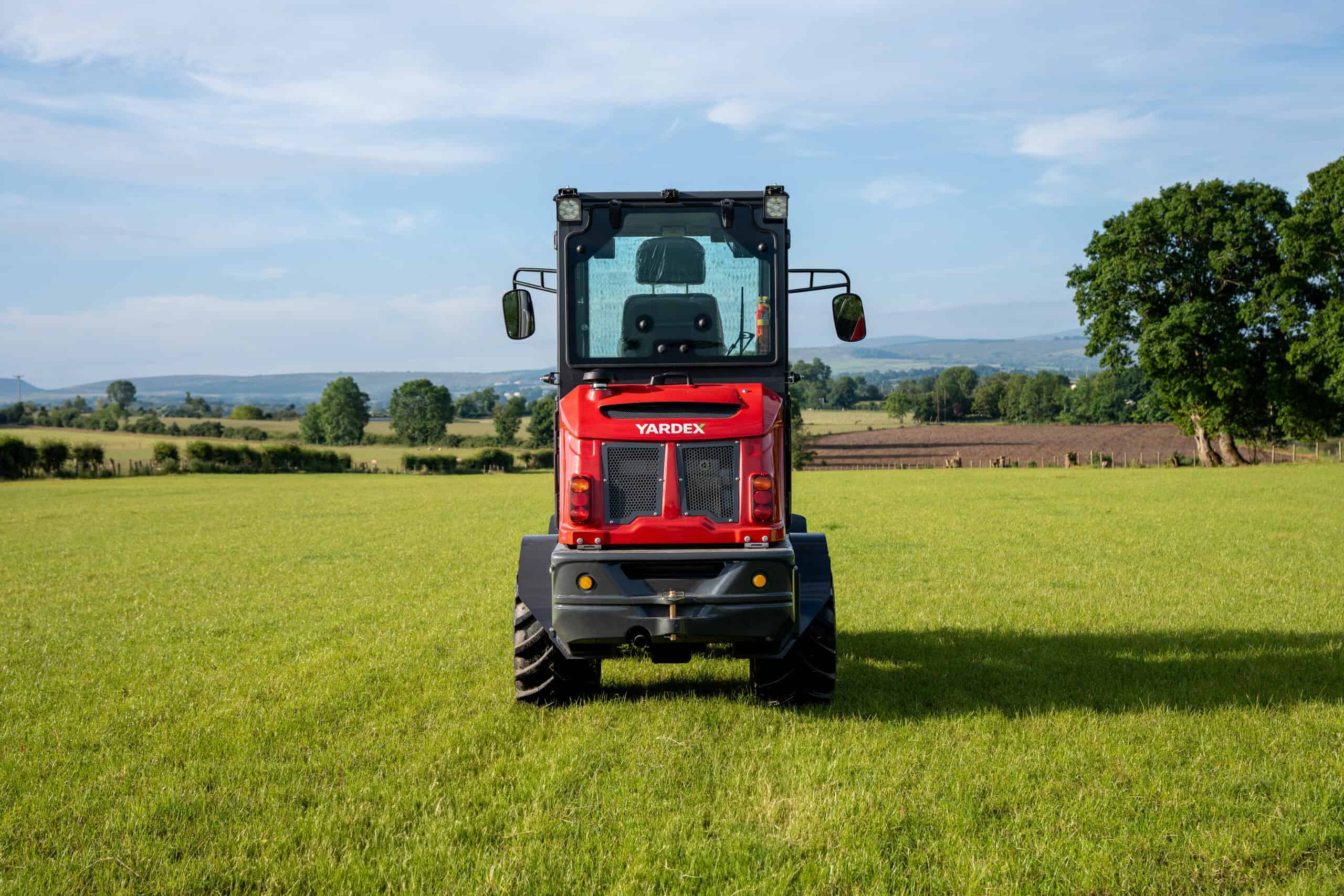 Red Yardex Group utility vehicle in a green field under blue sky.