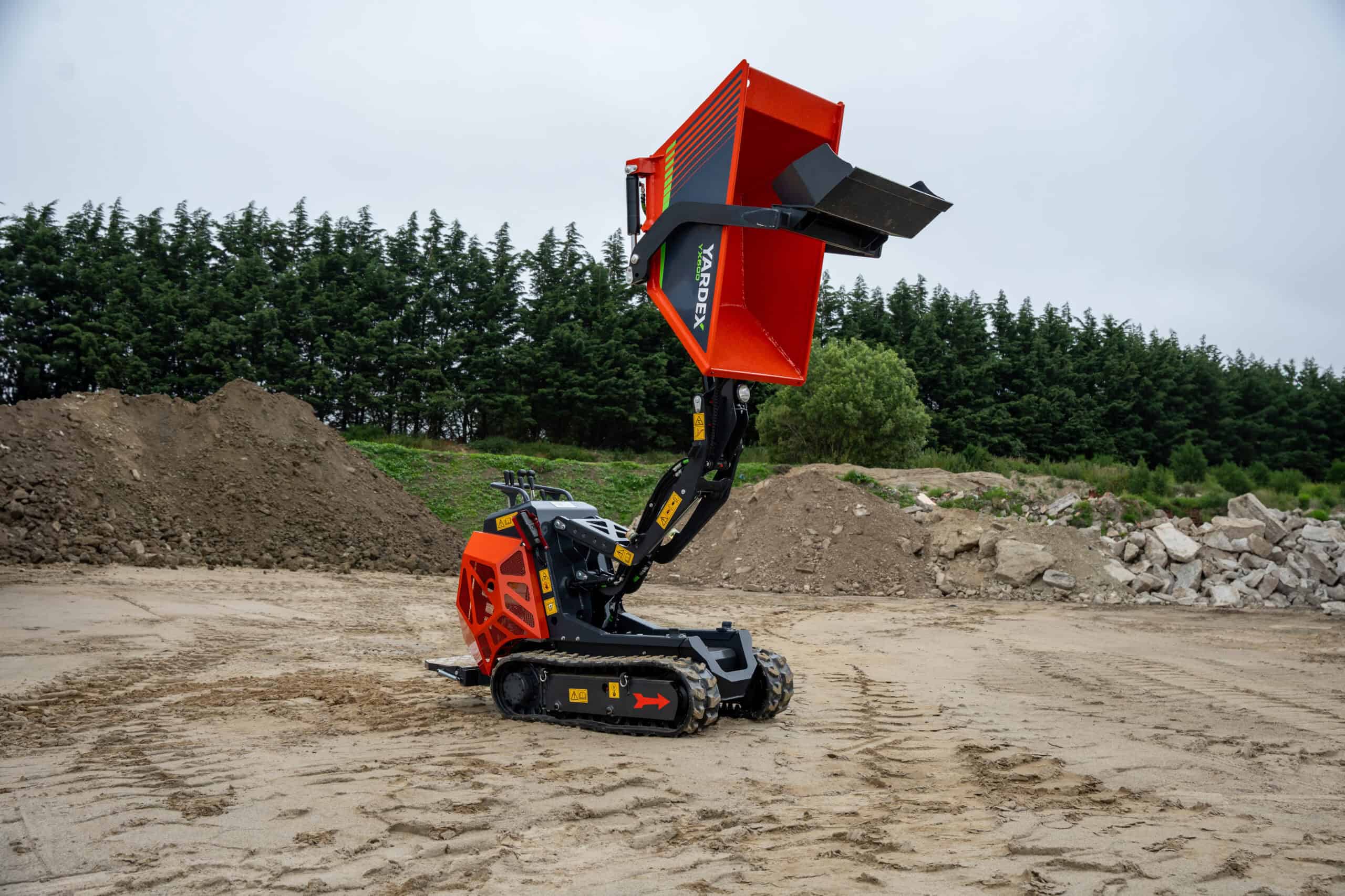 Compact skid steer loader with a large orange bucket at a construction site.
