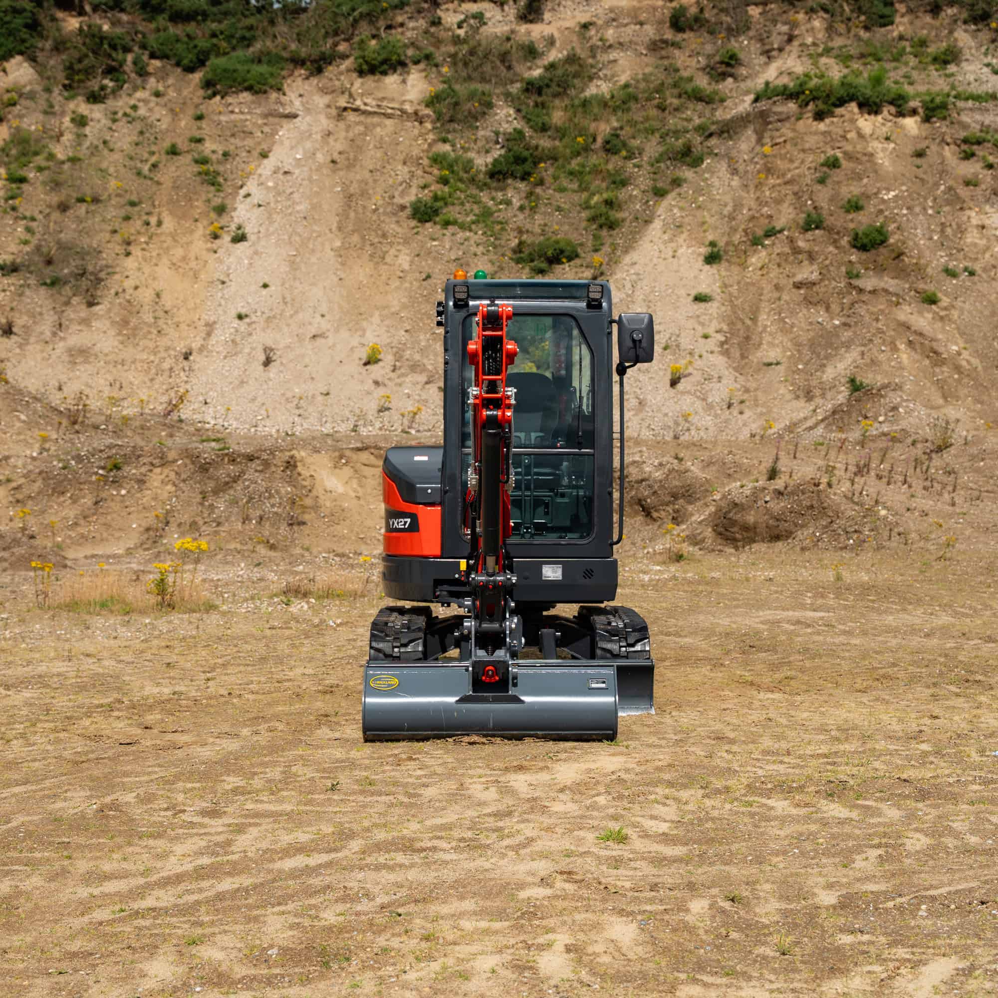 Small construction excavator on a dirt site with a hillside background.