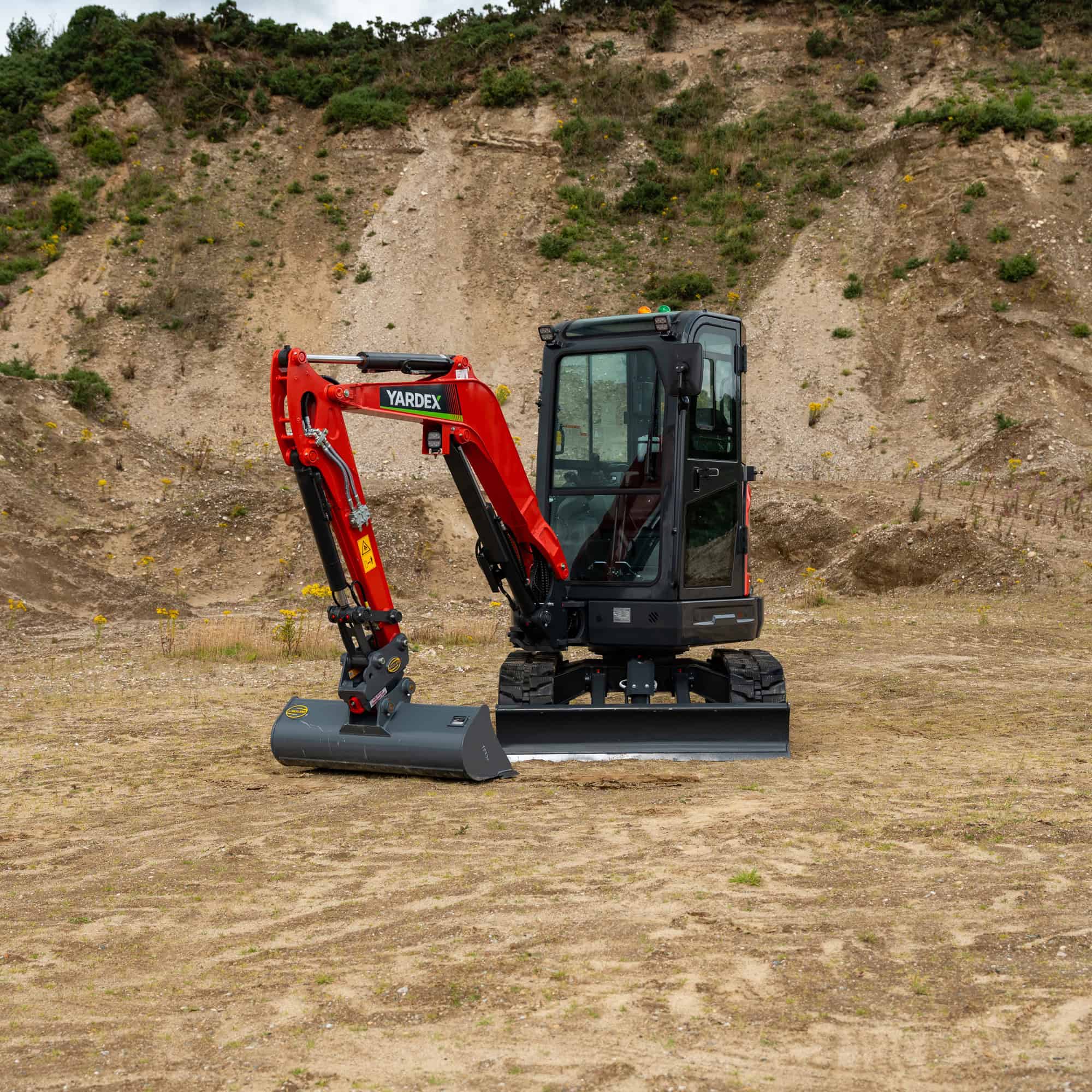 Yardex Group compact excavator working on a construction site with dirt and hills in background.