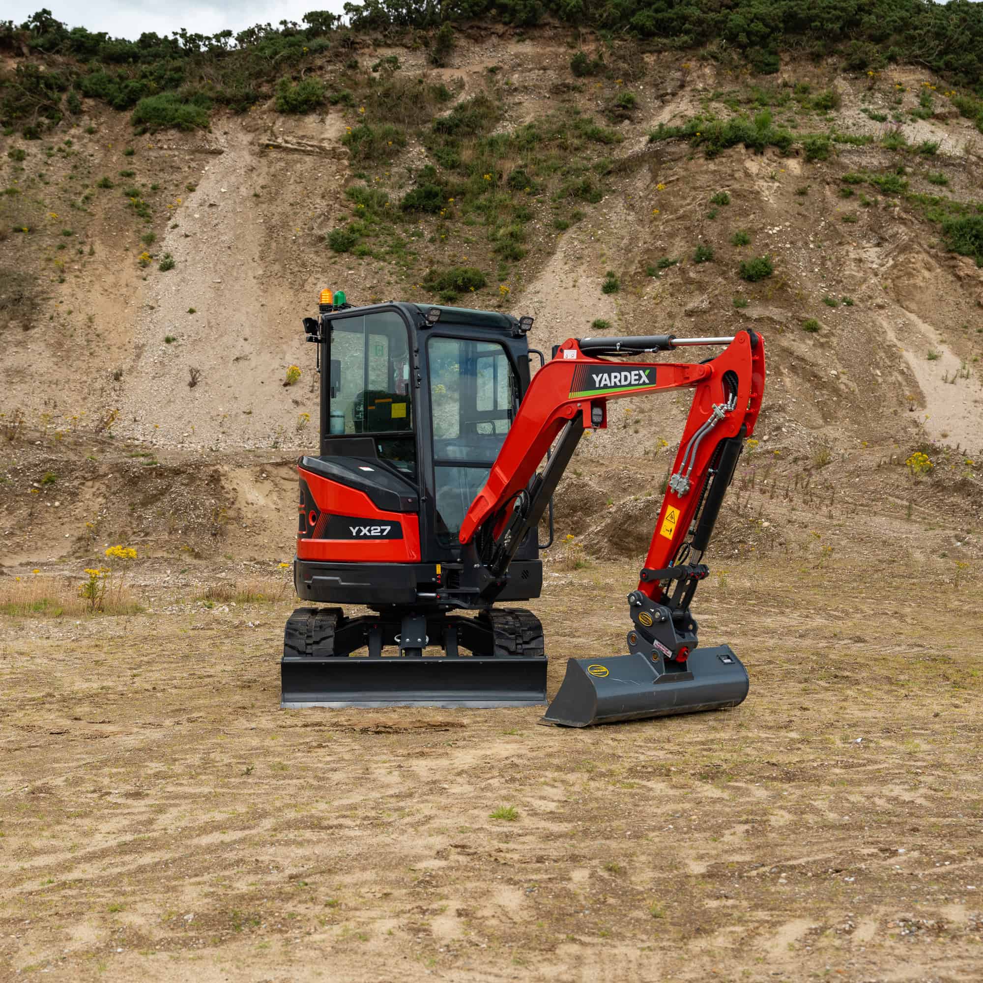 Yardex compact excavator on construction site with hillside background.