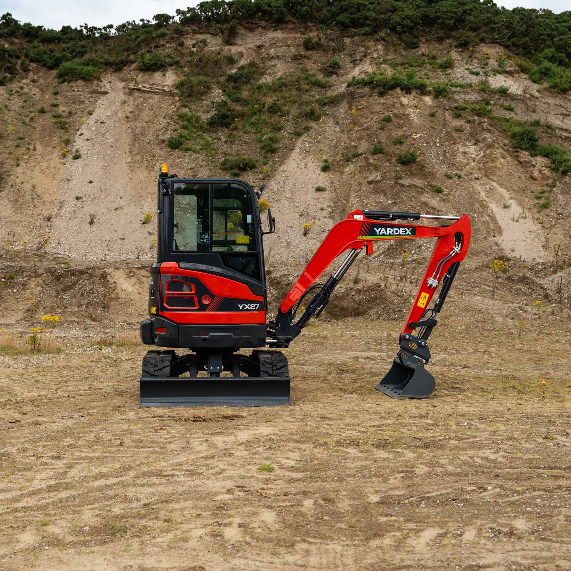 Yardex mini excavator working on a construction site with dirt and rocky terrain.