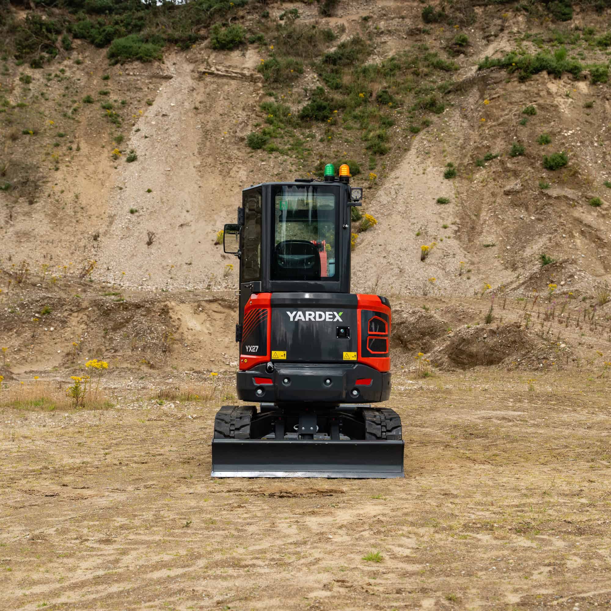 Yardex compact excavator on a construction site with dirt and hillside background.