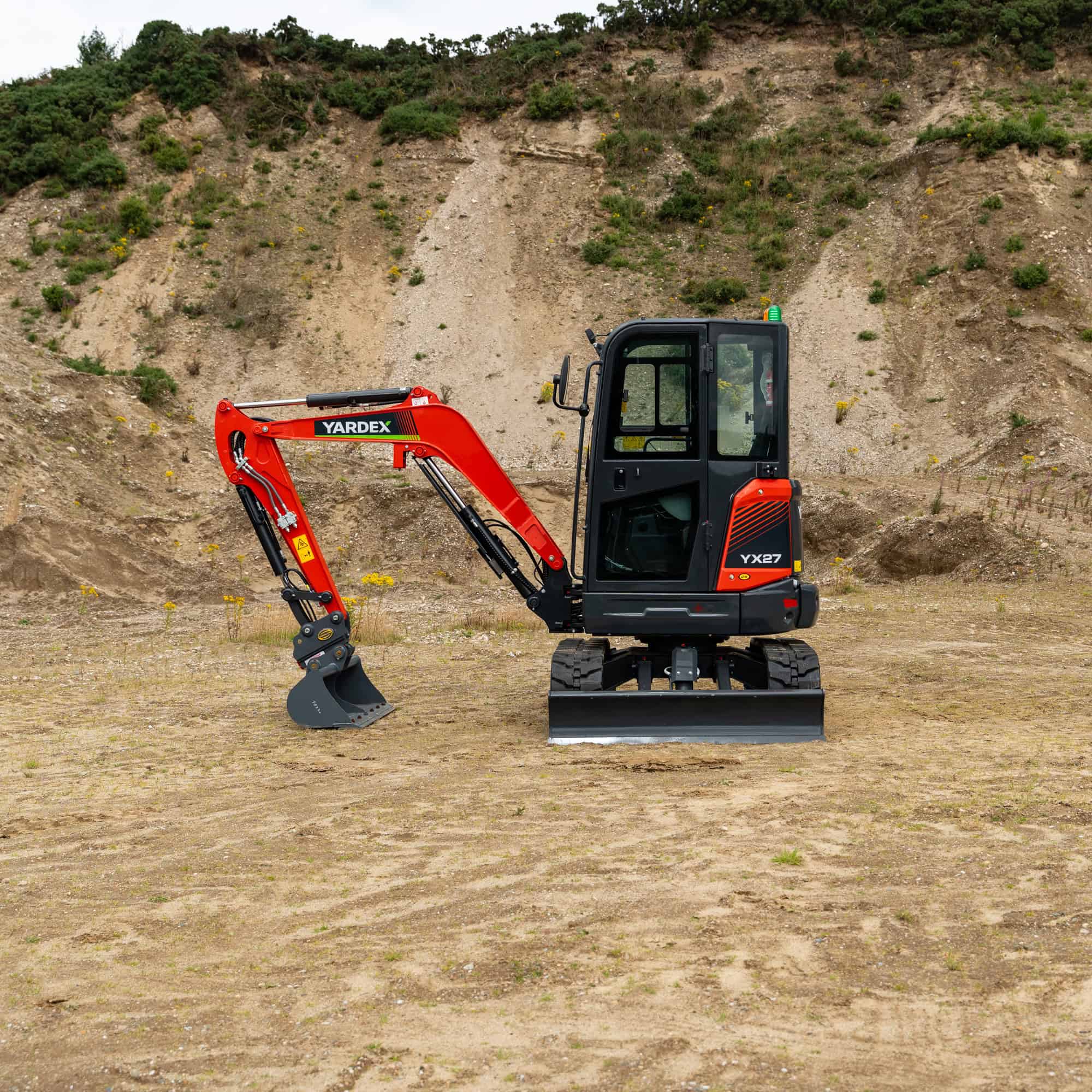 Yardex compact mini excavator on construction site with dirt and rocky background.