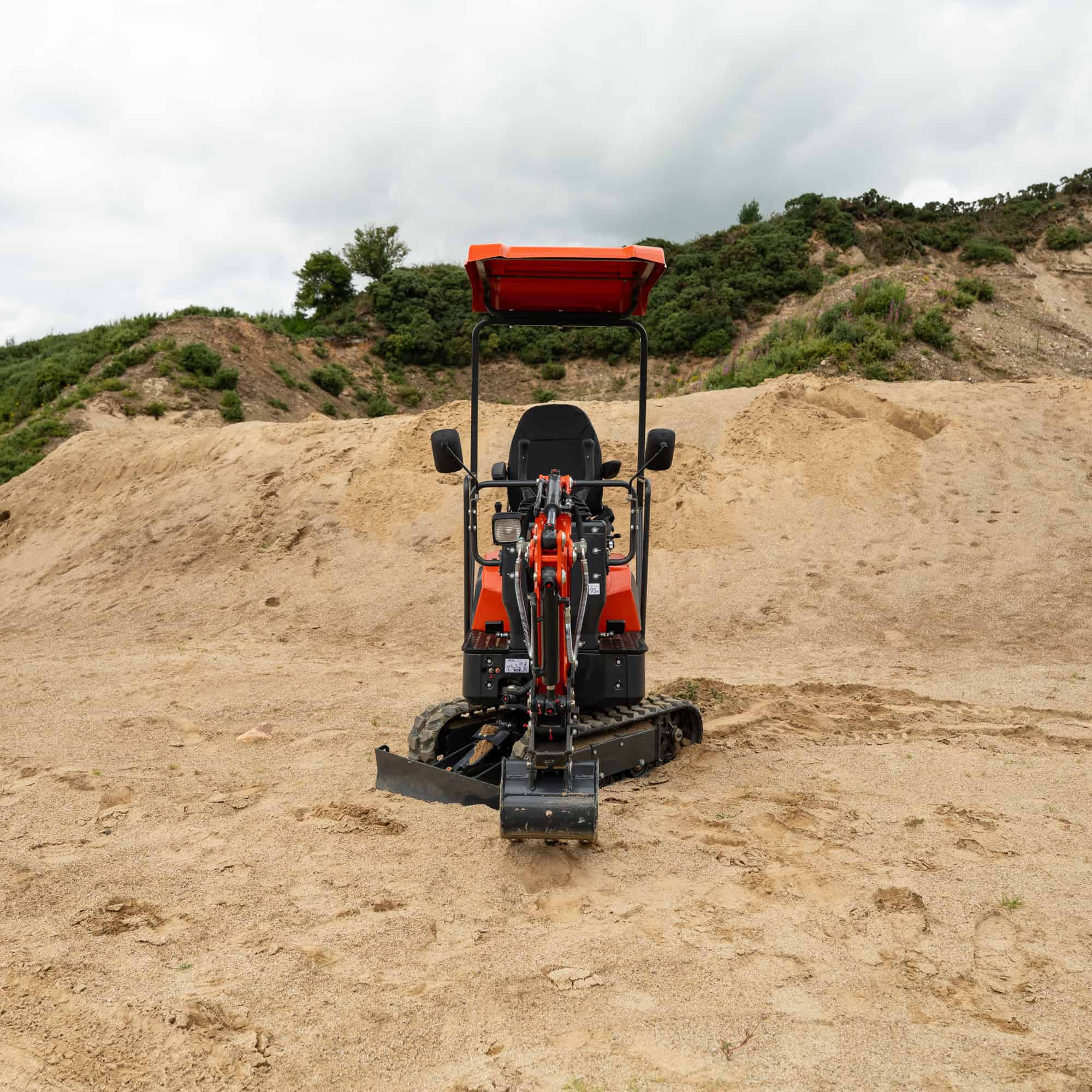 Compact excavator on a construction site with dirt and hills in background.