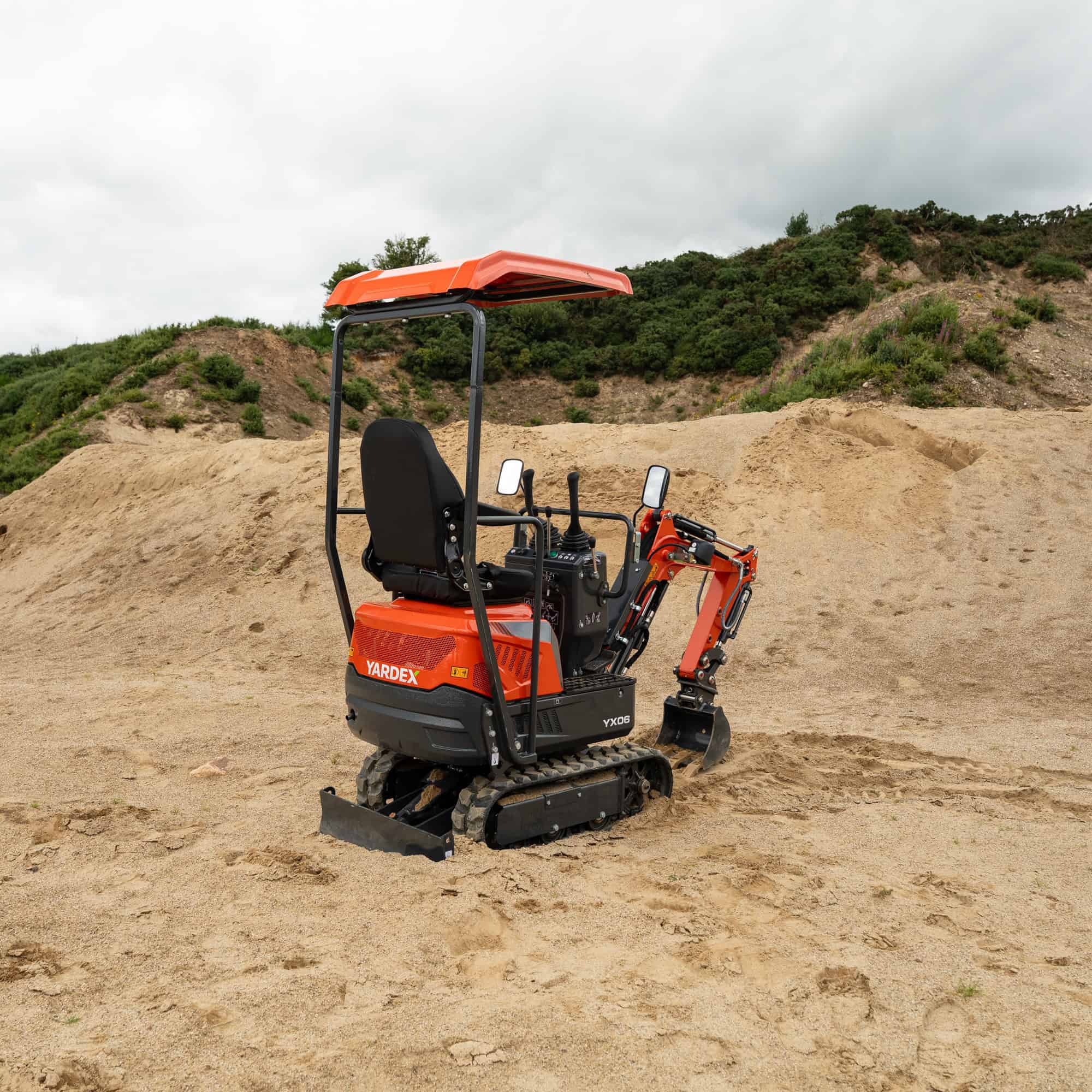 Yardex mini excavator working on sandy terrain with hills in background.