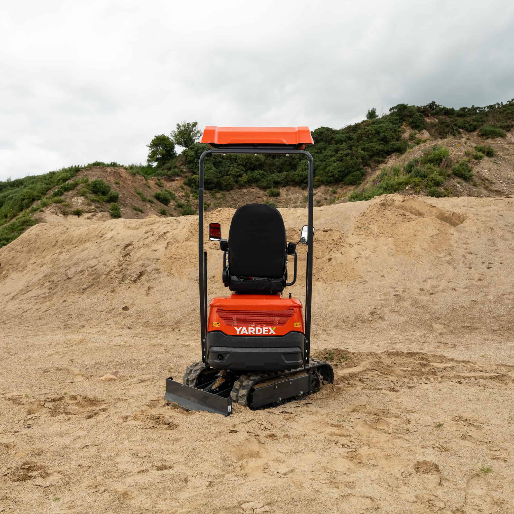 Yardex compact excavator working on a construction site with dirt and greenery.