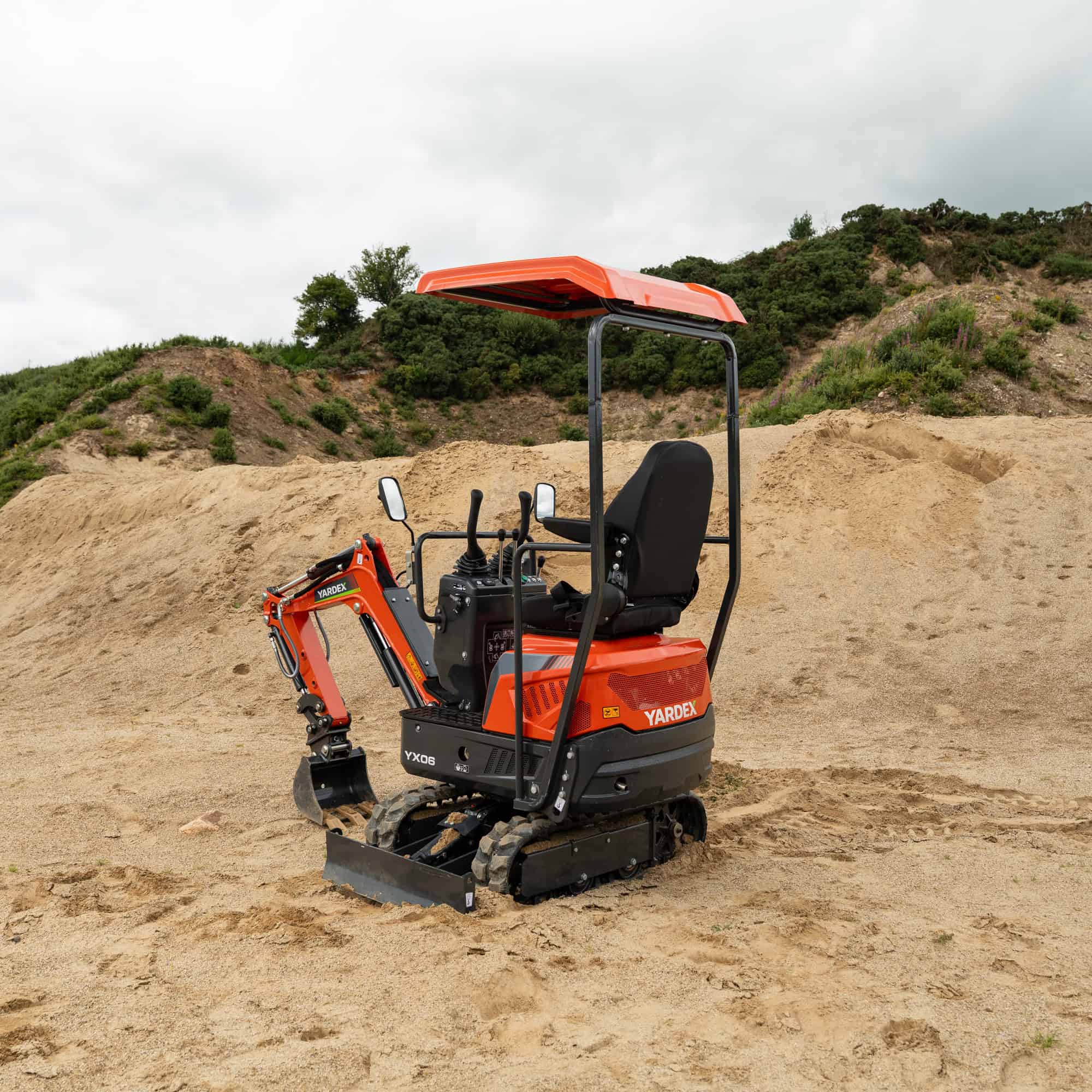 Yardex mini excavator on construction site with dirt and hills in background.