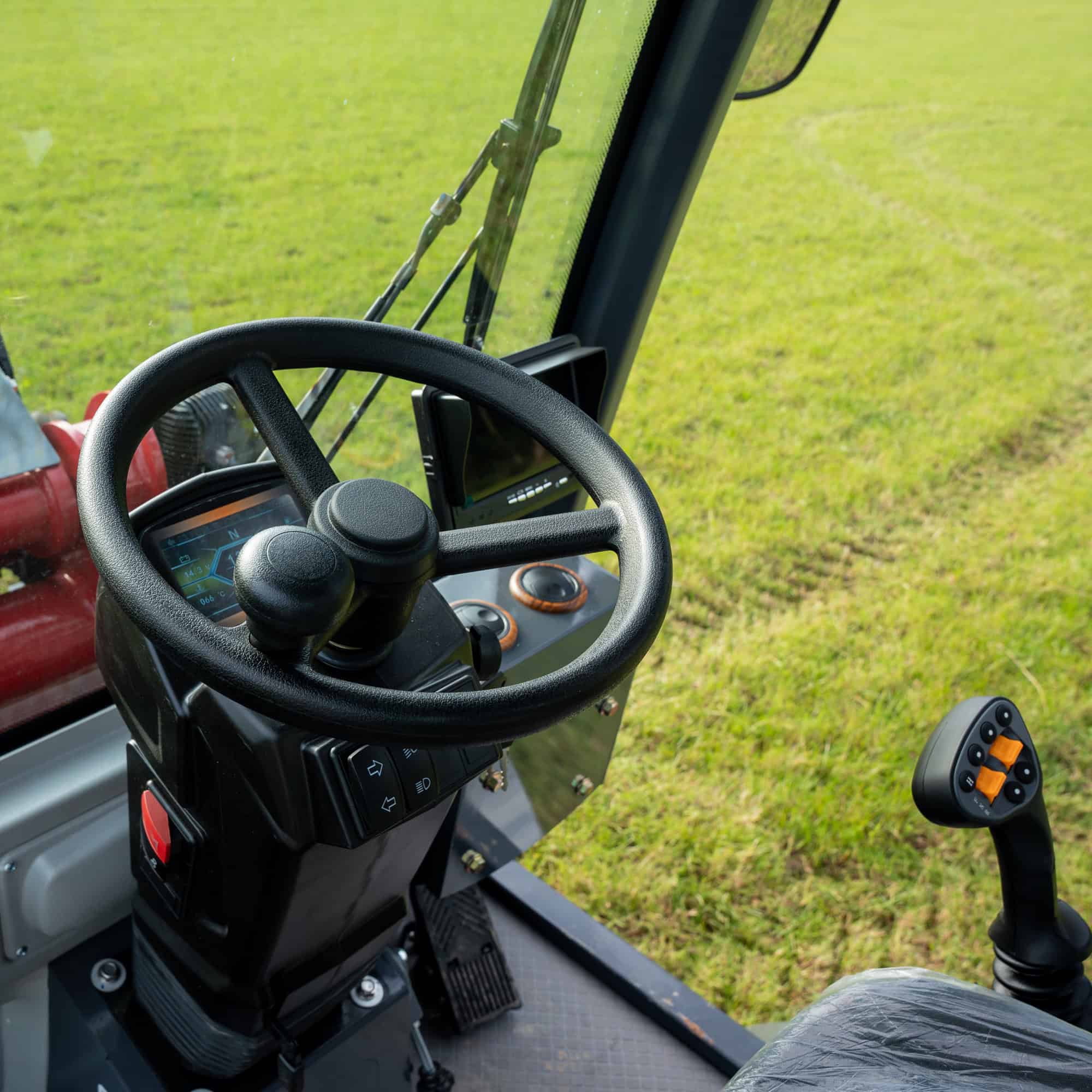 Close-up of tractor control panel with steering wheel and joystick on green field.
