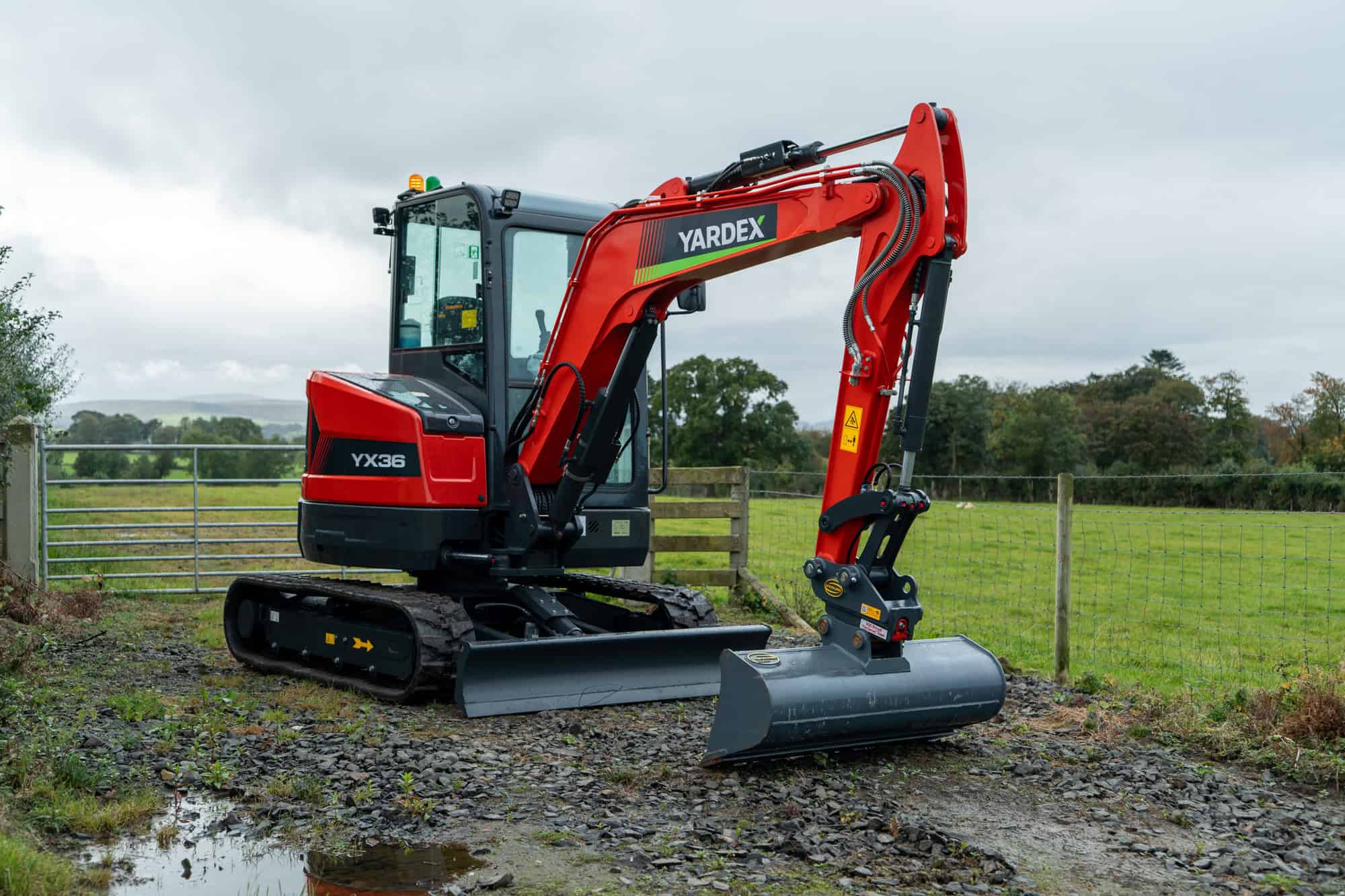 Red Yardex excavator on construction site with green field background.
