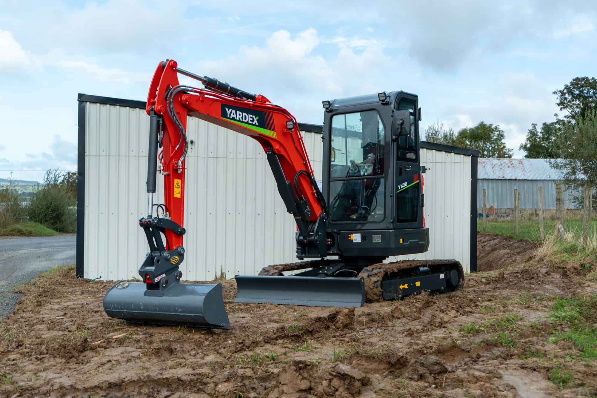 Red Yardex excavator on a construction site with dirt and sky background.